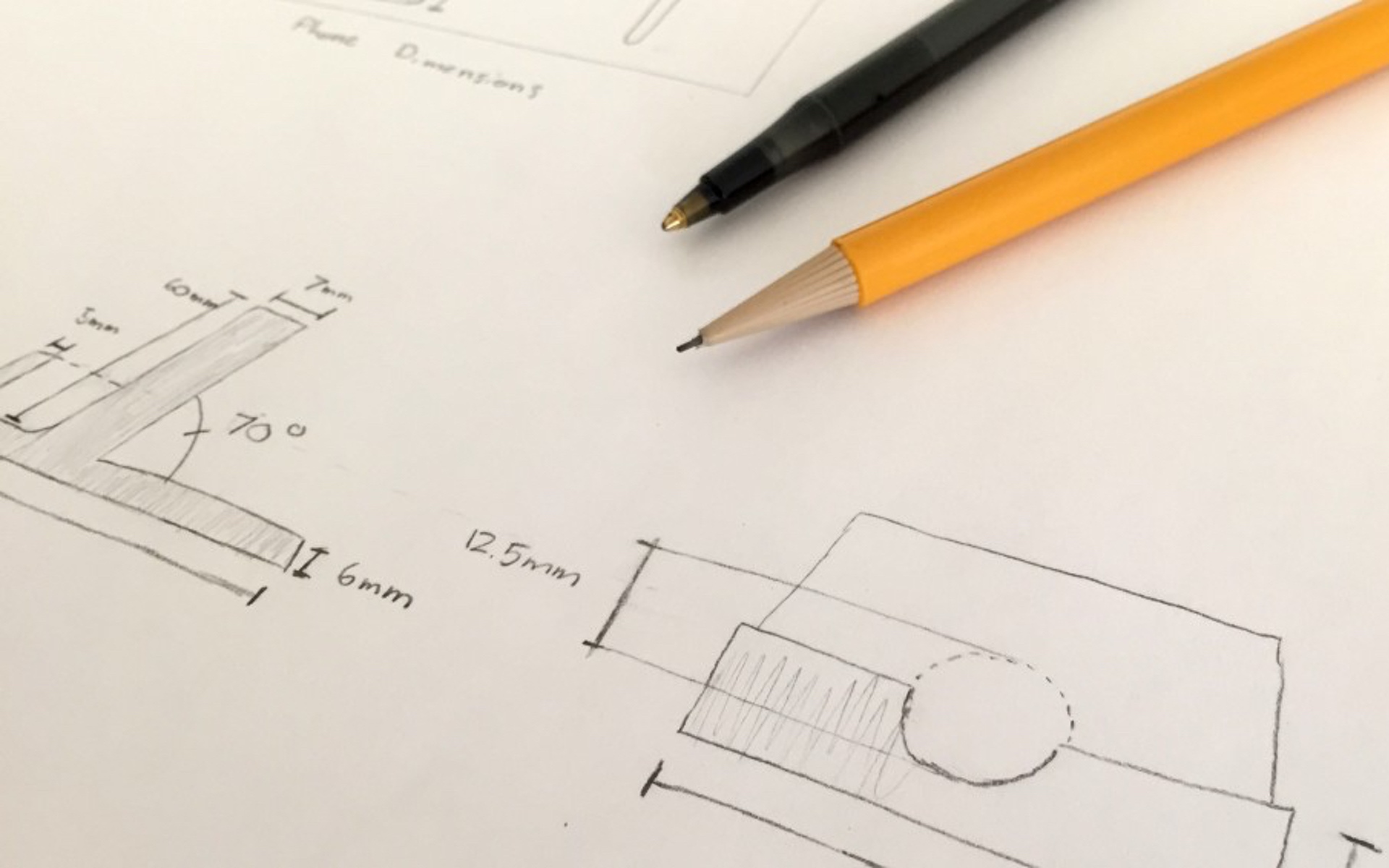 Various measurements and drawings of a phone stand with a pencil and pen sitting to the side